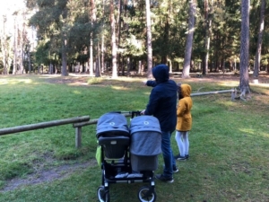 Frau mit einem Zwillingskinderwagen und einem weiteren Kind im Wald
