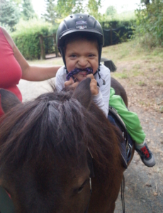Kleiner Junge mit Helm sitzt auf einem braunen Pony und beißt in den Zügel