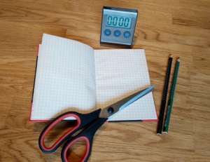 Ein Notizbuch mit Schere, zwei Buntstiften und eine Uhr auf einem Tisch